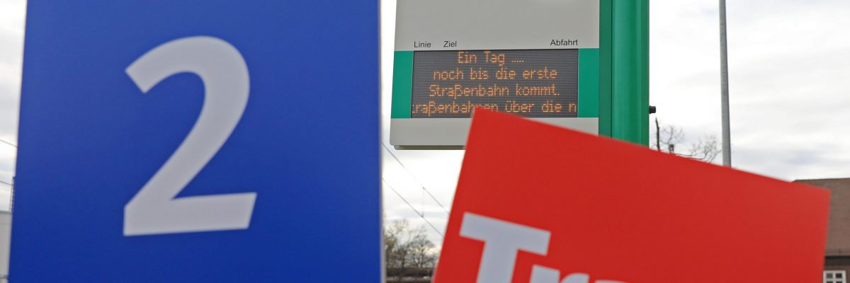 Zur Einweihung der neuen Strecke Puppentheater Bahnhof Buckau Warschauer Str. werden Schilder mit der Nummer 2 und dem Tram Logo vor der Fahrgastinformation an der Haltestelle S-Bhf. Buckau/Puppentheater in die Kamera gehalten.