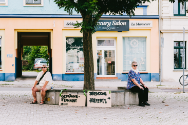 Wegweiser zur Gtränkefeinkost und zum Brewckau stehen an eine Bank gelehnt in Buckau