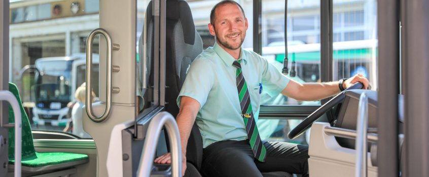 Busfahrer in Uniform sitzt im Bus und lächelt in die Kamera