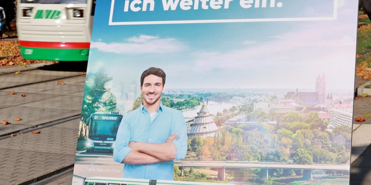 Jemand hält ein Plakat zu einer Klimaschutzaktion hoch Im Hintergrund ist eine Straßenbahn zu sehen.