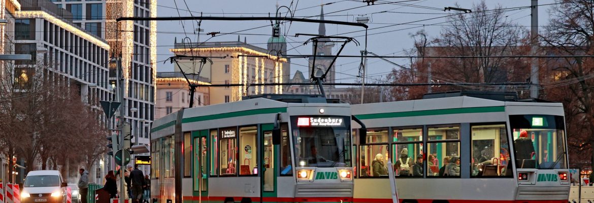 Straßenbahnen an der Haltestelle City Carré mit weihnachtlich beleuchteten Gebäude im Hintergrund.