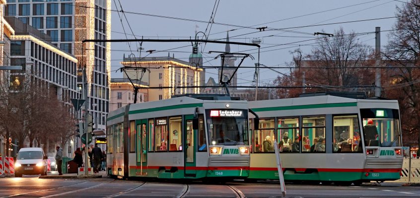 Straßenbahnen an der Haltestelle City Carré mit weihnachtlich beleuchteten Gebäude im Hintergrund.