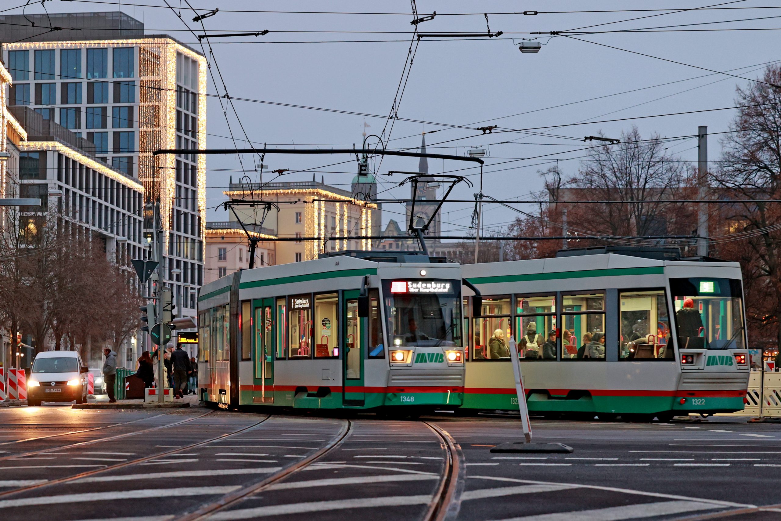 Straßenbahnen an der Haltestelle City Carré mit weihnachtlich beleuchteten Gebäude im Hintergrund.