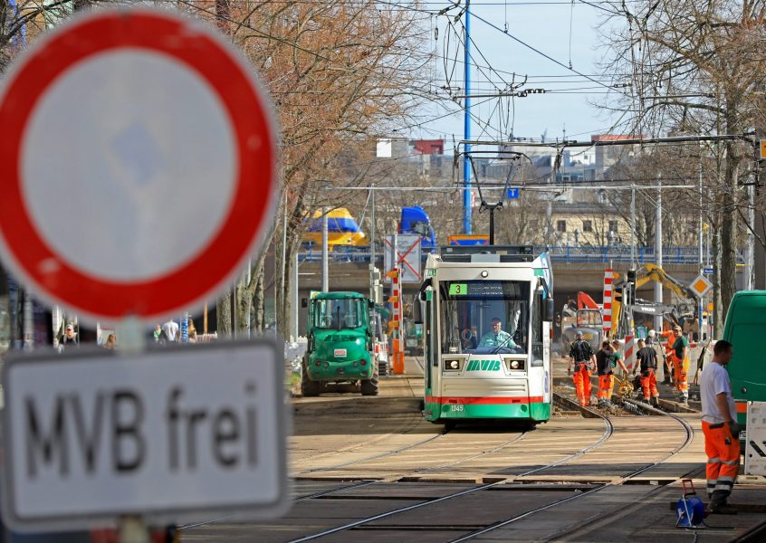 Straßenbahn der Linie 3 in einer Baustelle in der Olvenstedter Straße. Im Vordergrund ist unscharf ein "Durchfahrt verboten" Straßenschild mit dem Zusatzschild "MVB frei" zu sehen.