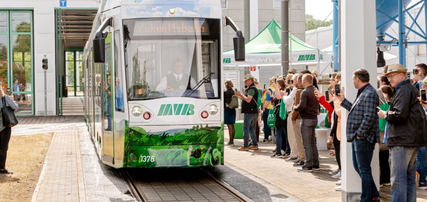 Die MVB-Zukunftsbahn fährt aus der Werkstatt. Publikum steht am Rand, applaudiert und filmt mit Handys.