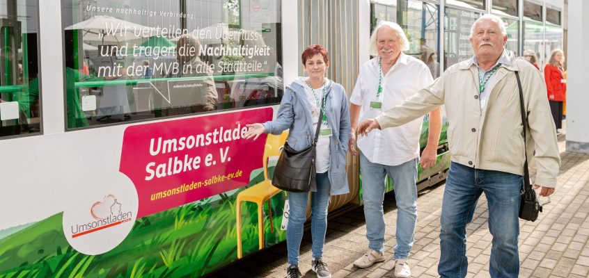 Vertreterinnen und Vertreter des Umsonstladen Salbke e.V. vor der mit Vereinen bedruckten Zukunftsbahn mit dem gleichnamigen Schriftzug