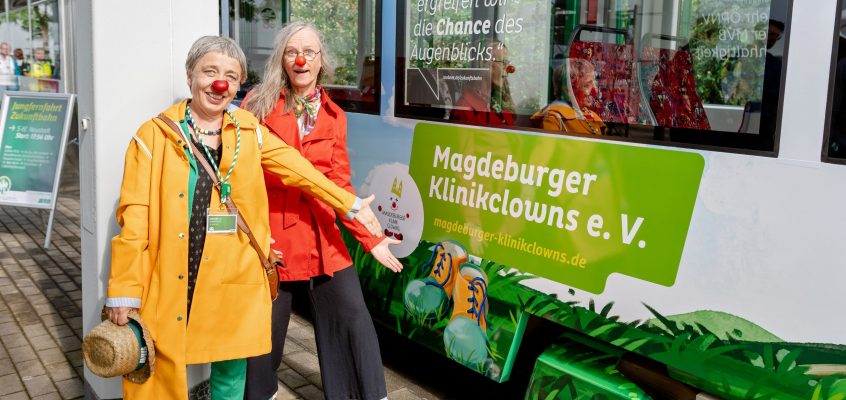 Vertreterinnen des Magdeburger Klinikclowns e.V. vor der mit Vereinen bedruckten Zukunftsbahn mit dem gleichnamigen Schriftzug