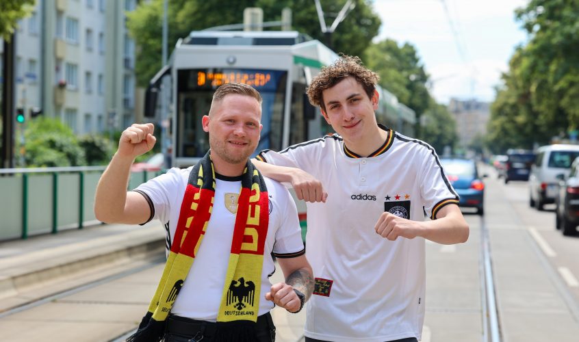 Zwei MVB Straßenbahnfahrer mit Deutschland Trikots vor einer Straßenbahn. Die Fahrer dürfen zur Heim Europameisterschaft das Trikot und nicht die Uniform tragen