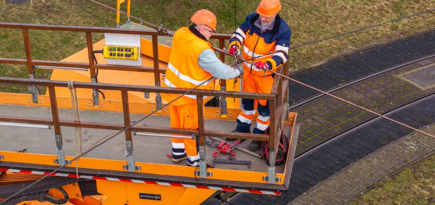 Zwei Männer arbeiten in Schutzkleidung an einer Oberleitung der Straßenbahn.