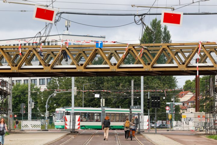 Behelfsbrücke für Autofahrer über dem Damaschkeplatz. Fußgänger laufen unter der Brücke durch und eine Straßenbahn fährt im Hintergrund.