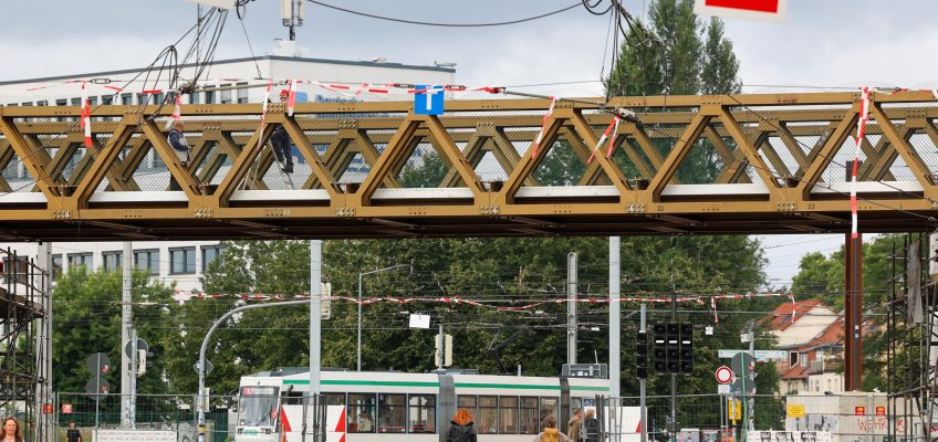 Behelfsbrücke für Autofahrer über dem Damaschkeplatz. Fußgänger laufen unter der Brücke durch und eine Straßenbahn fährt im Hintergrund.