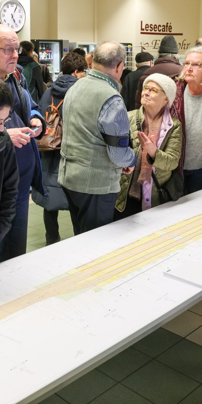 Planer und Bürger stehen an einem Tisch. Auf dem Tisch der Lageplan des Breiten Weges. Zwei Junge Männer betrachten detailiert den Plan.