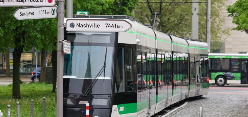 Die Flexity steht in der Hartstraße, ein Schild, auf dem die Partnerstädte der Stadt Magdeburg mit ihrer Entfernung abgebildet sind, steht im Verdergrund.