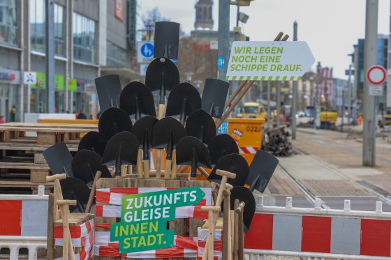 Kreativer Selfie-Spot „MVB-Baustellenthron“ am Breiten Weg in Magdeburg. Der aus Paletten und zahlreichen schwarzen Spaten gestaltete Thron trägt die Schilder „Zukunftsgleise Innenstadt.“ und „Wir legen noch eine Schippe drauf.“ Im Hintergrund sind die Baustelle am Breiten Weg, Straßenbahngleise und Baufahrzeuge zu sehen.