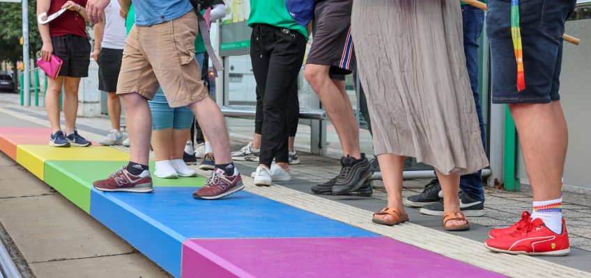 Bahnsteig mit Menschen in Regenbogenfarben.