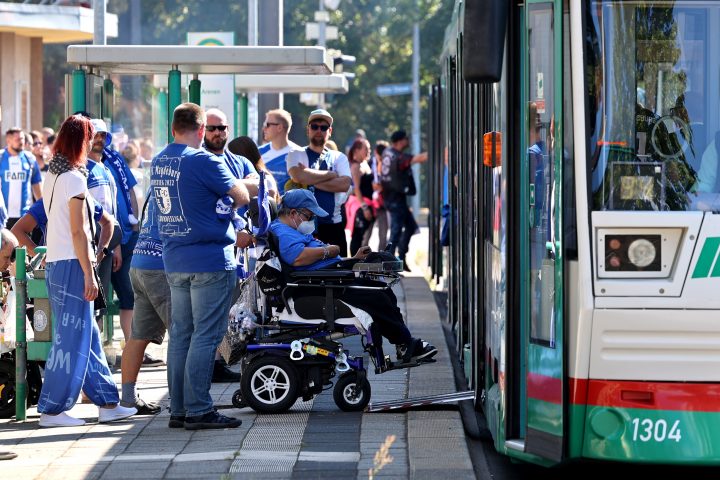 Straßenbahn steht an der Haltestelle Arenen. An der Haltestelle stehen viele FCM Fusßballfans in blau weiß.