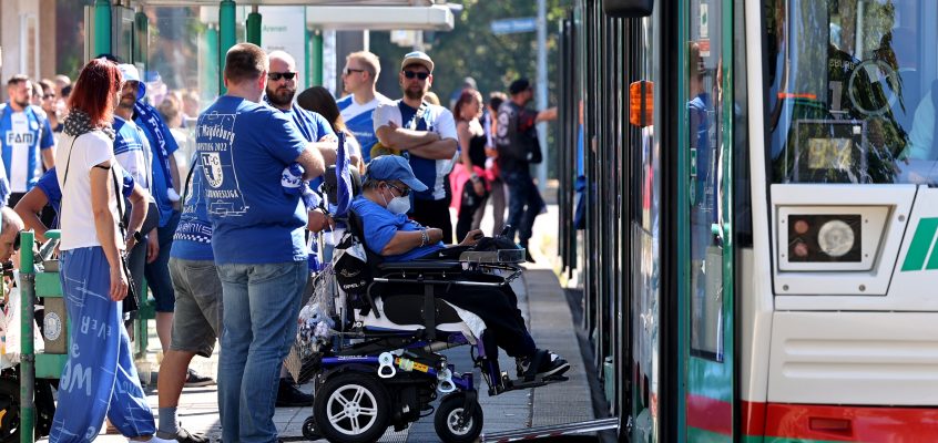 Straßenbahn steht an der Haltestelle Arenen. An der Haltestelle stehen viele FCM Fusßballfans in blau weiß.