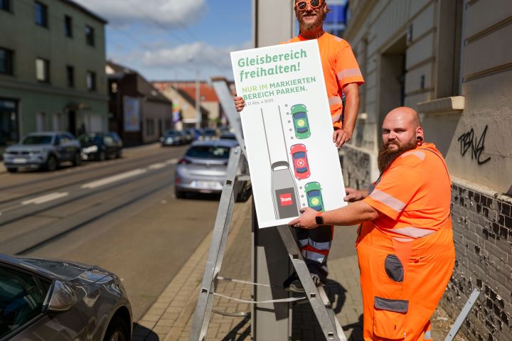 Zwei Mitarbeiter der MVB montieren ein Hinweisschild gegen Falschparker.