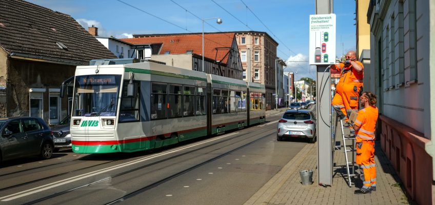 Straßenbahn in der Genthiner Straße. Rechts zwei Mitarbeiter der MVB, die ein Hinweisschild montieren.